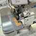 Close-up of a Juki industrial serger sewing machine in silver and white, actively sewing Denim. Juki MO-6700 Series overlock sewing machine. MO6704S 0F6 50H: 1 Needle(3 Threads) Overlock | 4.8mm 3 rolls | Medium-Heavy Running Stitch(Denims) | Extra High Throw